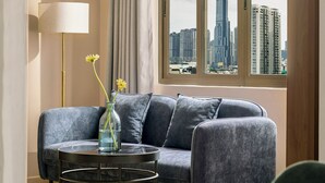 Un salón moderno con un sofá gris, una mesa redonda de centro y una lámpara de pie. Un ventanal ofrece vistas a un horizonte urbano.