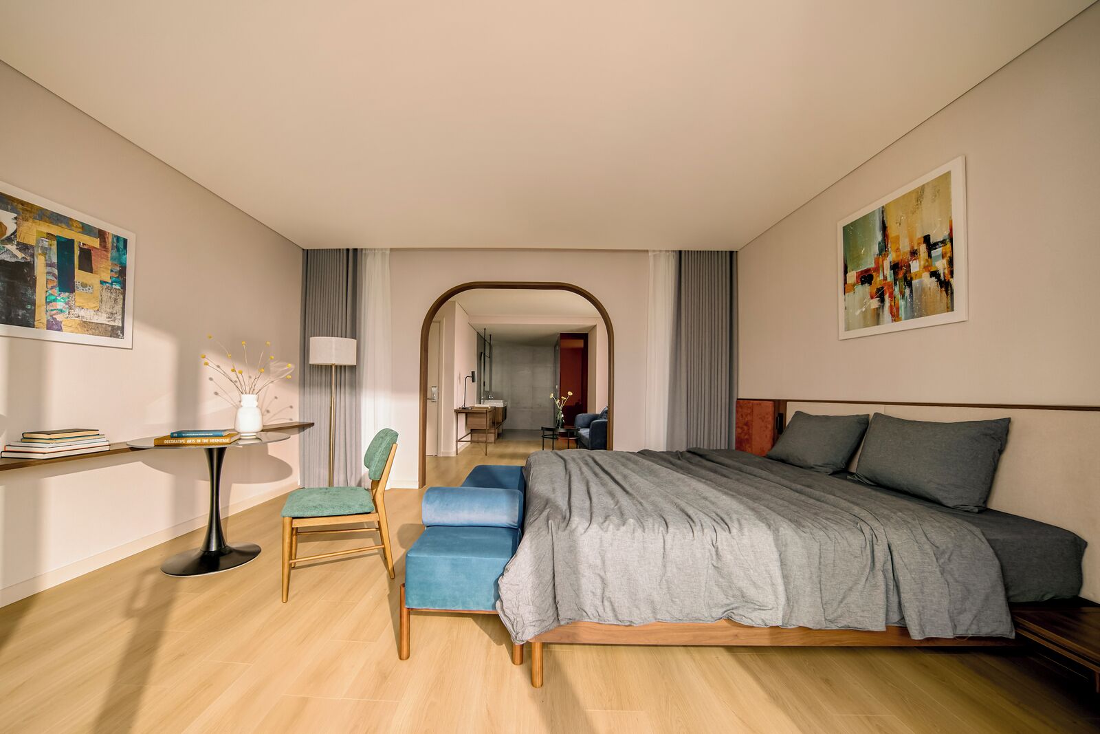 Quarto de hotel moderno com uma cama grande, uma mesa e uma cadeira. Há um corredor que dá para um banheiro e uma área de estar.