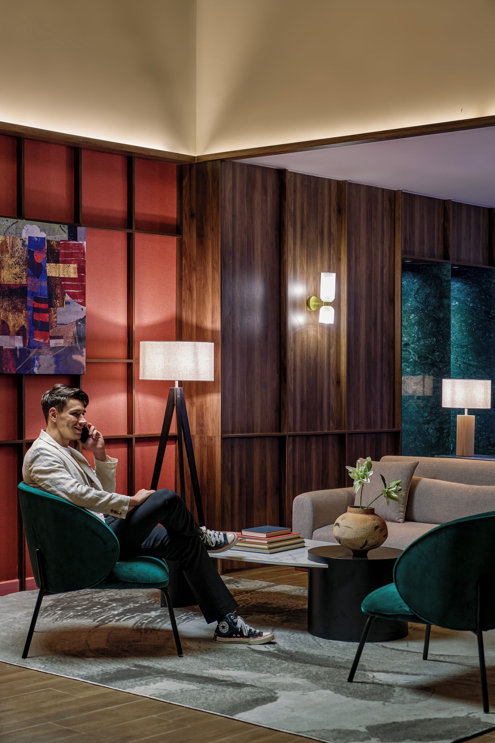 A modern living room with a person seated on a green chair, a sofa, a coffee table, and a floor lamp.