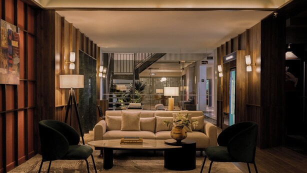 Un moderno vestíbulo de hotel con una zona de estar central, una escalera y vistas al interior.