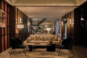 A modern hotel lobby with a central seating area, a staircase, and a view of the interior.