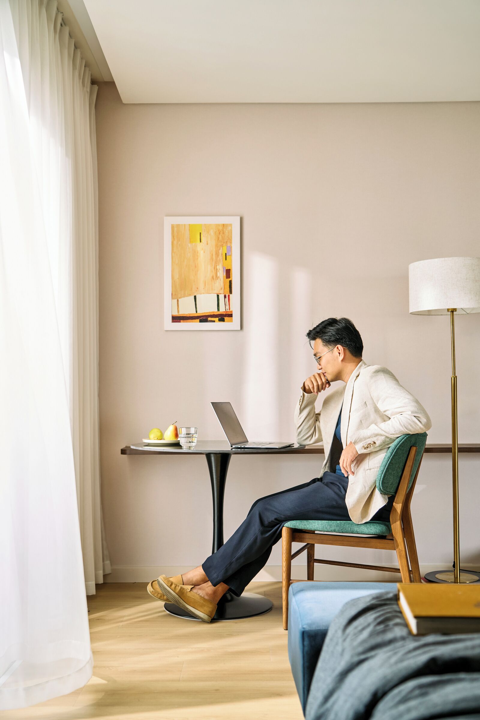 A man sitting on a chair at a desk with a laptop, a plate of fruit, and a glass of water.