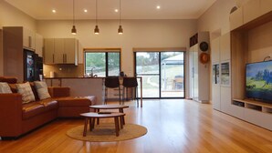 Ein modernes Wohnzimmer mit einer Couch, einem Couchtisch und einem Fernseher. Es gibt eine Küchenzeile mit Schränken und einen Essbereich mit Stühlen.