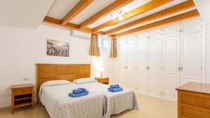 A bedroom with a wooden headboard, two beds with patterned bedding, a nightstand, a desk, and a wardrobe.