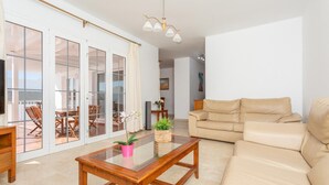 A spacious living room with a beige sofa, a glass coffee table, and a dining area with a table and chairs.