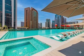 Ein Pool auf dem Dach mit Liegestühlen, Blick auf hohe Gebäude und einem klaren Himmel.