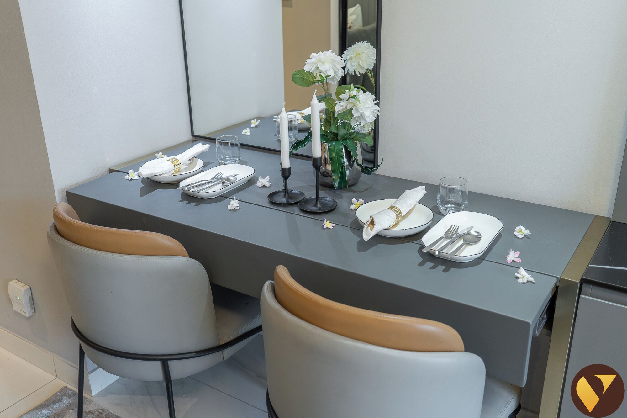 A dining table set with white plates, silverware, and a vase of white flowers.