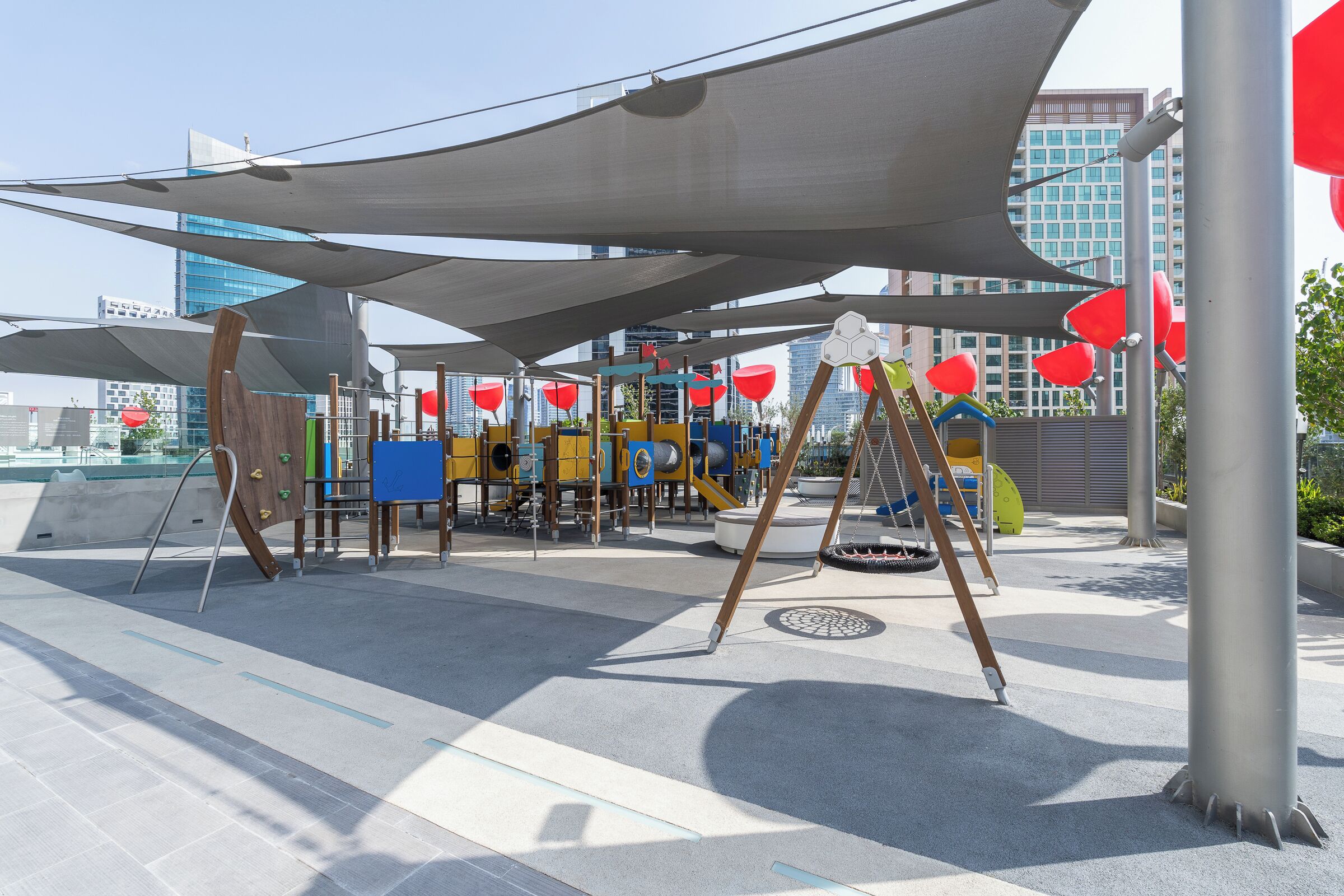 An outdoor play area with shaded structures, a slide, and a climbing wall.