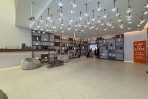 Eine großzügige Lobby mit modernem Design, ausgestattet mit einer zentralen Sitzecke, einer Treppe und einem Café-Schild.