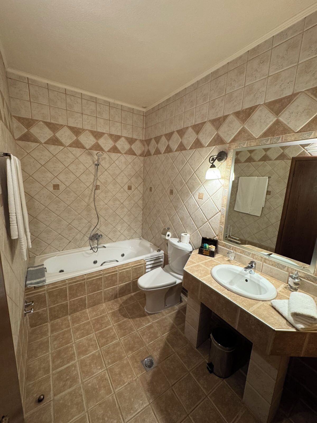 A bathroom with a bathtub, toilet, and sink, featuring beige tiles and a mirror.