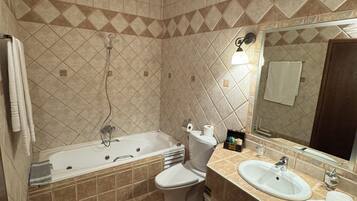 A bathroom with a bathtub, toilet, and sink, featuring beige tiles and a mirror.