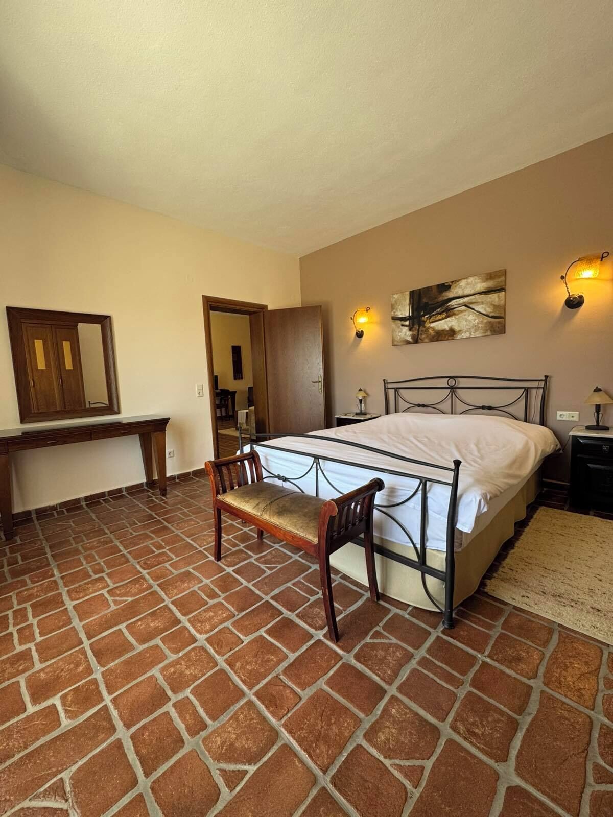 Un dormitorio con una cama, un banco de madera, un escritorio y un espejo.