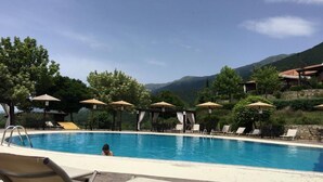 A swimming pool with lounge chairs and umbrellas, surrounded by trees and mountains. - Hotel Epavlis (Sintiki)