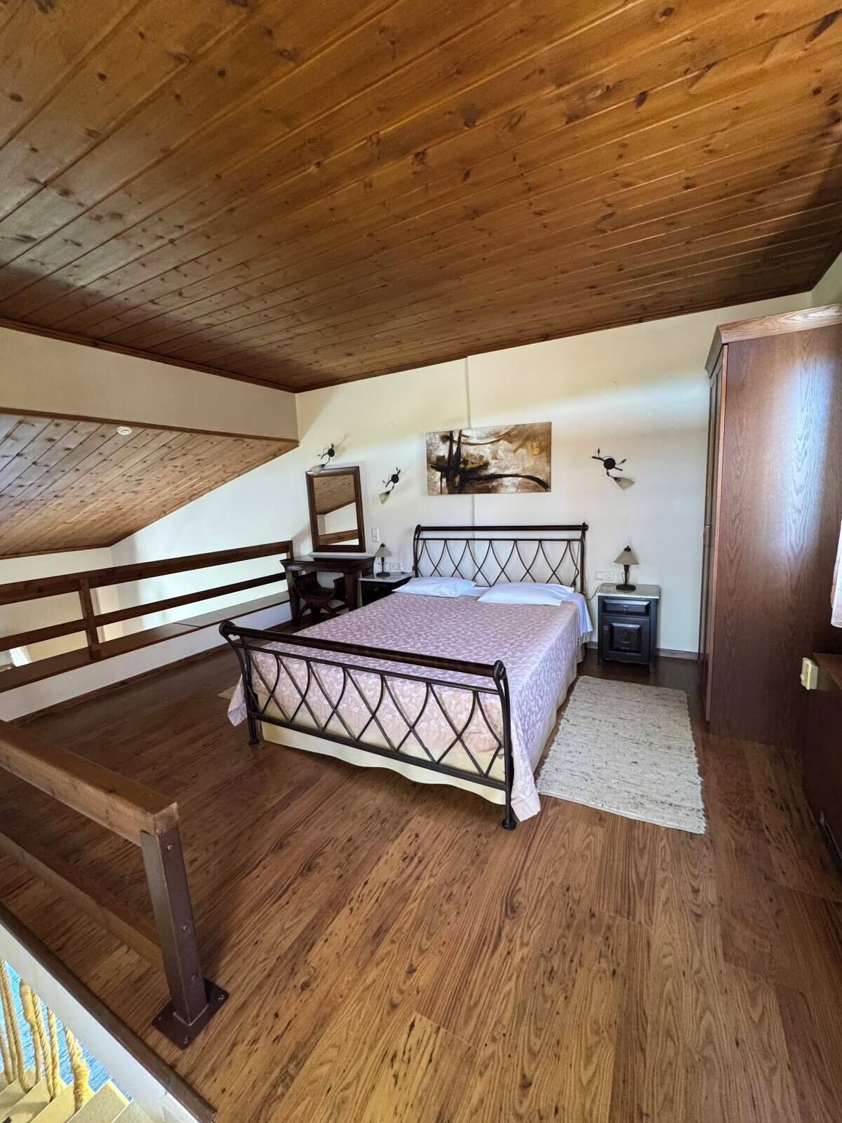 Quarto com teto de madeira, cama com estrutura de metal, mesa de cabeceira e guarda-roupa.