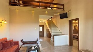 Un vaste espace de vie doté d’un plafond en bois, d’un escalier menant à l’étage supérieur et d’un téléviseur à écran plat fixé au mur.