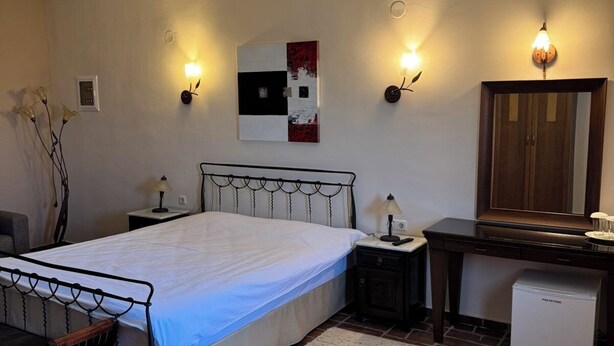 A bedroom with a bed, bedside tables, a desk, a refrigerator, and a wall-mounted artwork. - Hotel Epavlis (Sintiki)