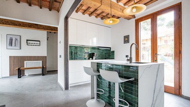 A modern kitchen with a green backsplash, white cabinets, and a marble island with bar stools.