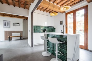 Una cocina moderna con un revestimiento verde, armarios blancos y una isla de mármol con taburetes.
