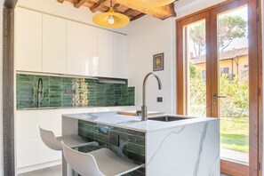 A modern kitchen with a marble island, a green backsplash, and a wooden ceiling. - Welcome to the “Little House in the Garden” of Villa Sania! The annex is located near the sunny beach, just a short walk from the Pinewood; here you can enjoy the peaceful coolness of the surrounding green park and have an unforgettable experience in (Viareggio)