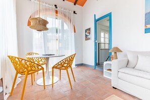 A dining area with a round table and yellow chairs, a white sofa, and a view through a blue door. - Welcome to the “Little House in the Garden” of Villa Sania! The annex is located near the sunny beach, just a short walk from the Pinewood; here you can enjoy the peaceful coolness of the surrounding green park and have an unforgettable experience in (Viareggio)