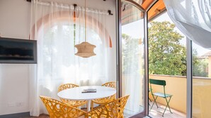 A balcony with a table and chairs, a hanging light fixture, and a view of trees through a glass door.