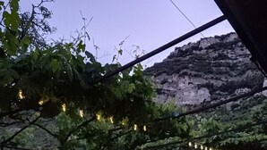 Een bank onder een pergola met lichtslingers, een gazon en een bergachtige achtergrond.