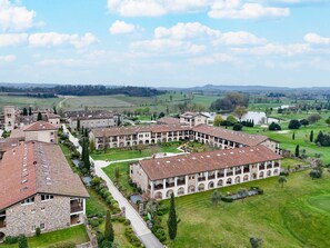 A historic building complex with multiple buildings, courtyards, and surrounding green fields.