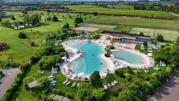 A resort with two large swimming pools, a golf course, and lush greenery.
