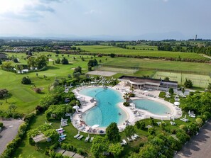 Een resort met twee grote zwembaden, een golfbaan en weelderige begroeiing.
