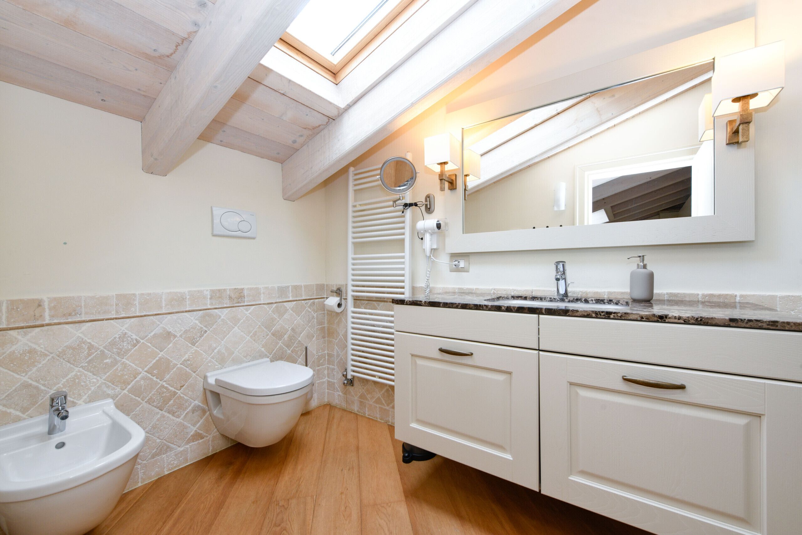 Une salle de bain dotée d’un puits de lumière, d’un bidet, de toilettes, d’un meuble-lavabo avec un miroir et d’un porte-serviettes.