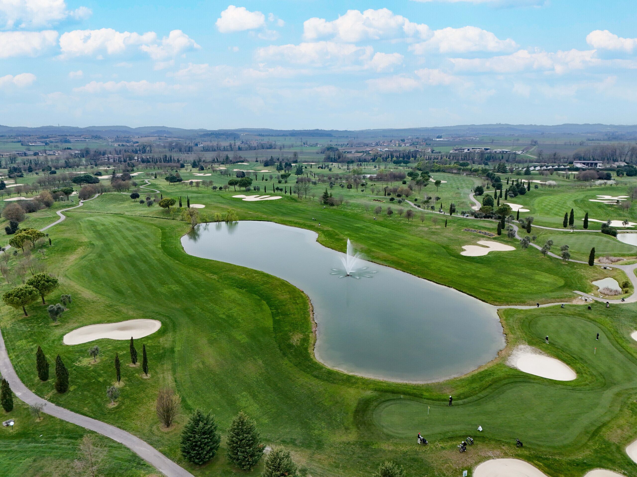 A golf course with a pond, sand bunkers, and a fountain.