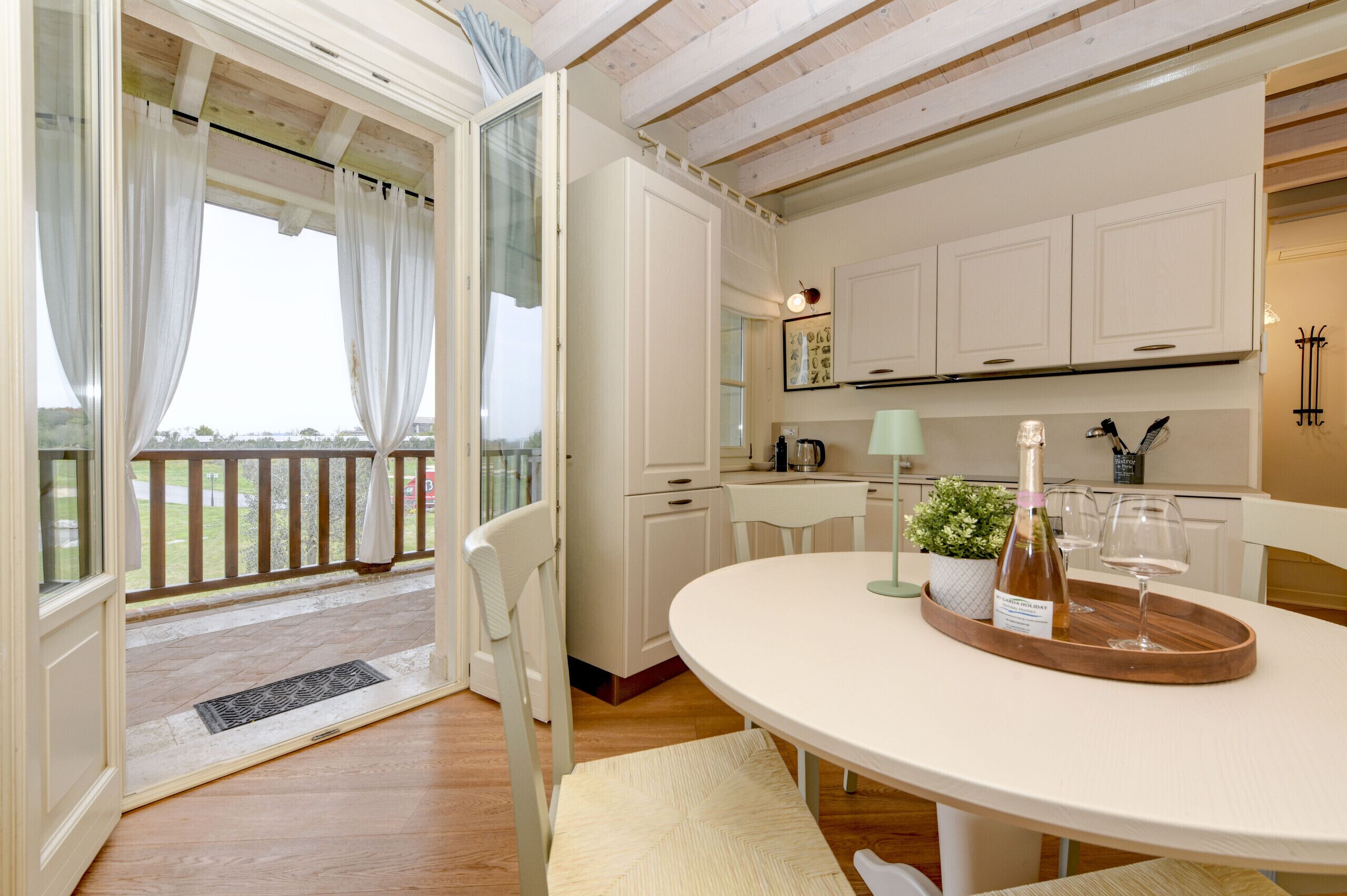 Een moderne keuken met witte kastjes, een eettafel met een wijnfles en glazen, en uitzicht door een glazen deur op een buitenruimte.
