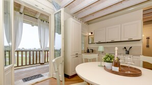 A modern kitchen with white cabinets, a dining table with a wine bottle and glasses, and a view through a glass door to an outdoor area.