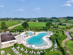 A large, circular swimming pool with multiple lounge areas and a surrounding lawn.