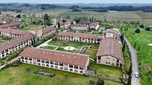 An aerial view of a historic building complex with multiple courtyard buildings, surrounded by green fields and distant hills.