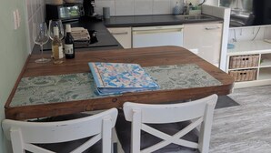 A kitchen with white cabinets, a black countertop, and a wooden dining table with two white chairs. - The corner house (Egmond aan Zee)