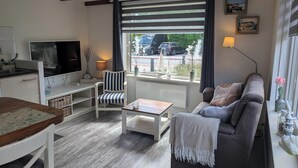 A cozy living room with a sofa, a striped chair, a coffee table, and a TV. - The corner house (Egmond aan Zee)