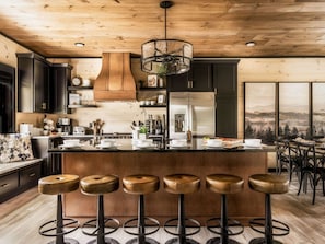 A modern kitchen with a central island, bar stools, and a large window with a scenic view.