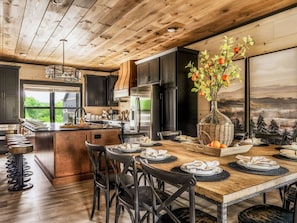 A modern kitchen with dark cabinets, a central island, and a dining area with chairs and a table set for a meal.