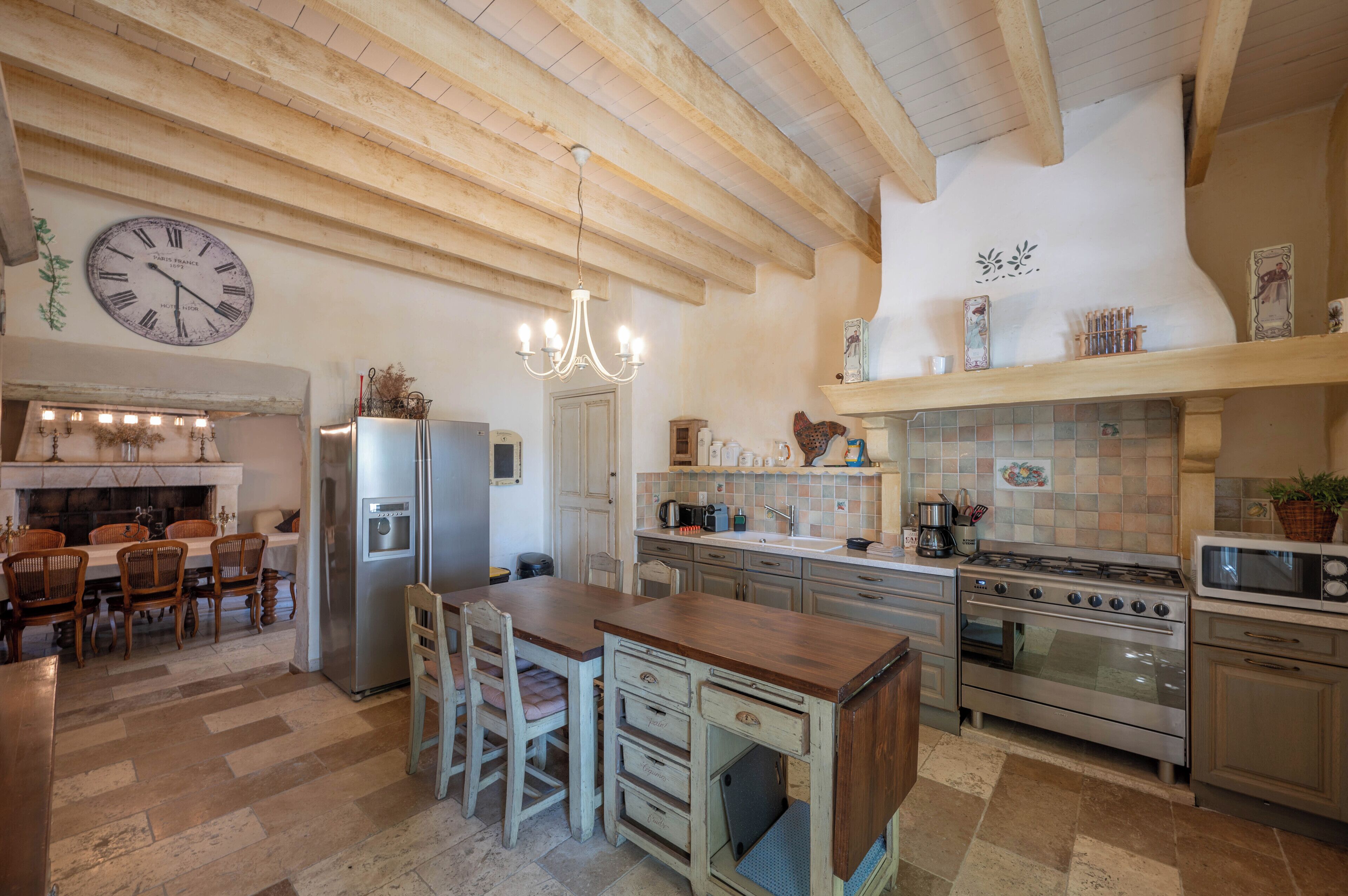 A kitchen with wooden beams, a chandelier, a clock, and a tiled backsplash.