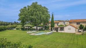 Un prato curato con piscina e lettini, circondato da edifici in pietra e un grande albero.