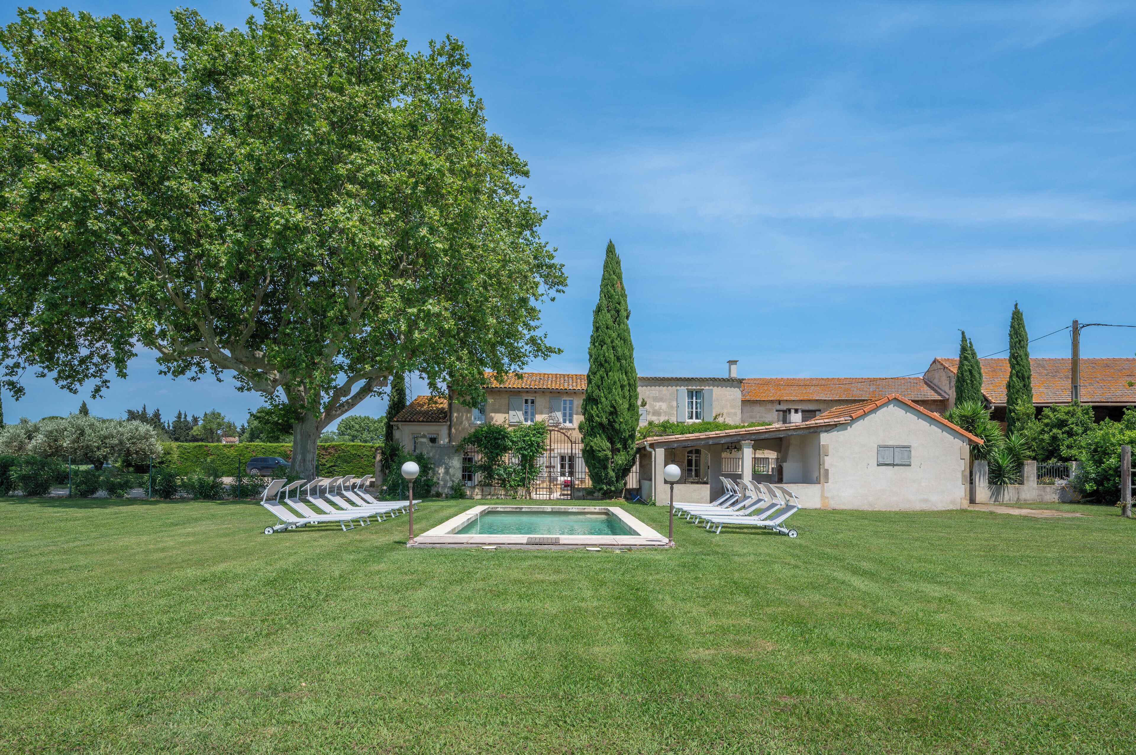 A villa with a swimming pool, surrounded by a well-maintained lawn and trees.