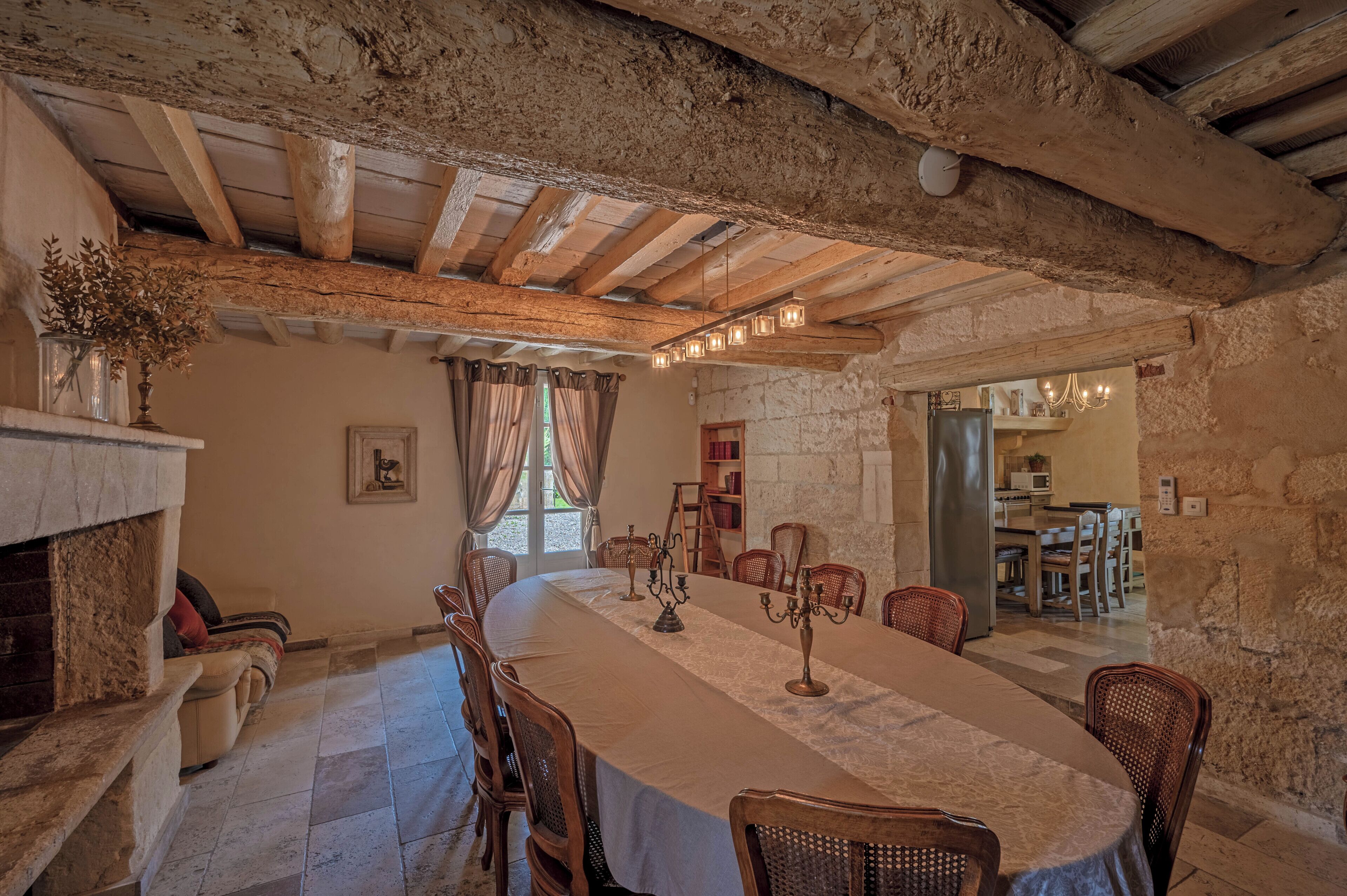 Un comedor rústico con una mesa larga, sillas de madera, una chimenea, paredes de piedra y vigas de madera a la vista.