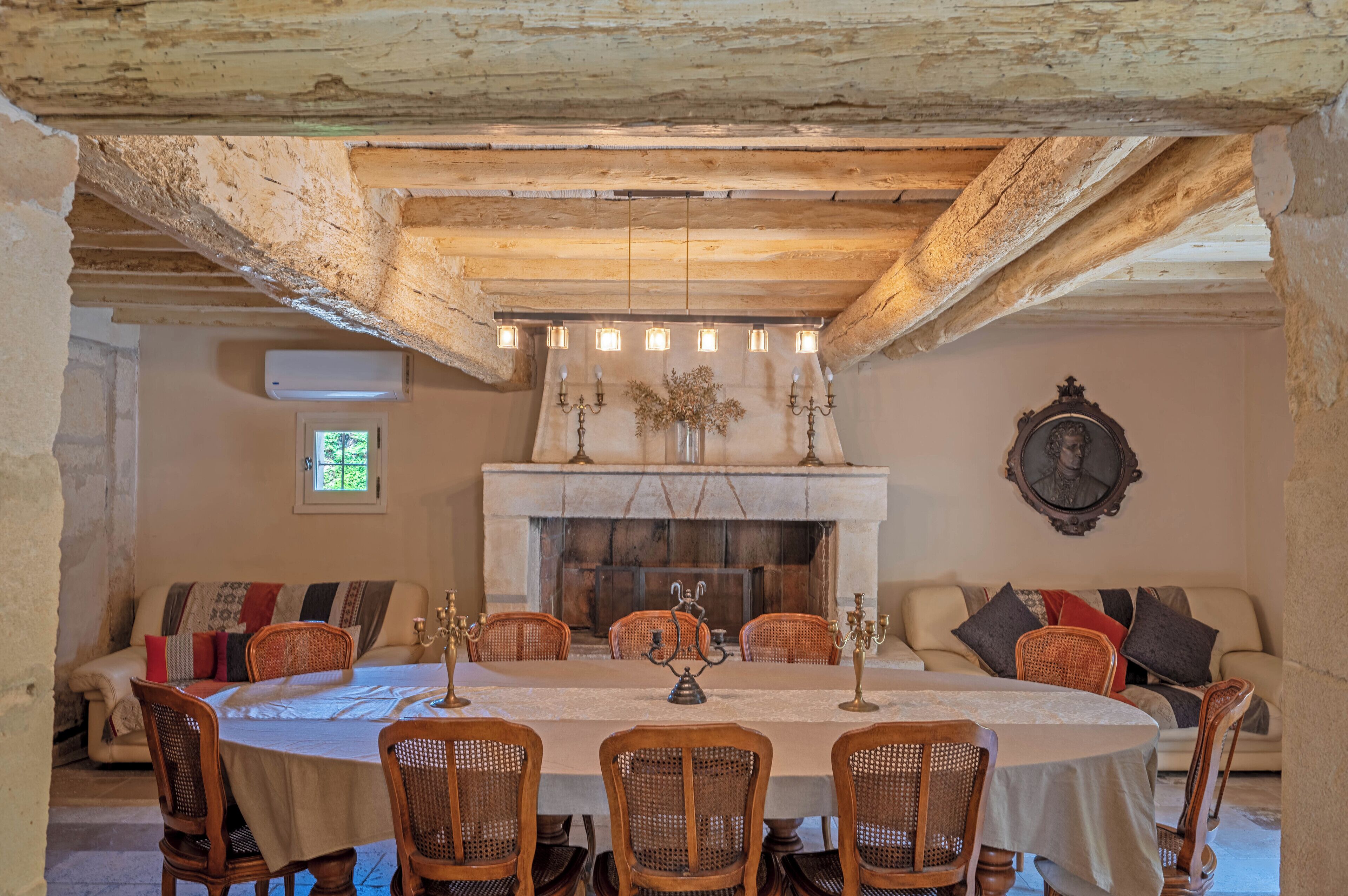 A dining room with a round table, wooden chairs, a fireplace, and a chandelier.