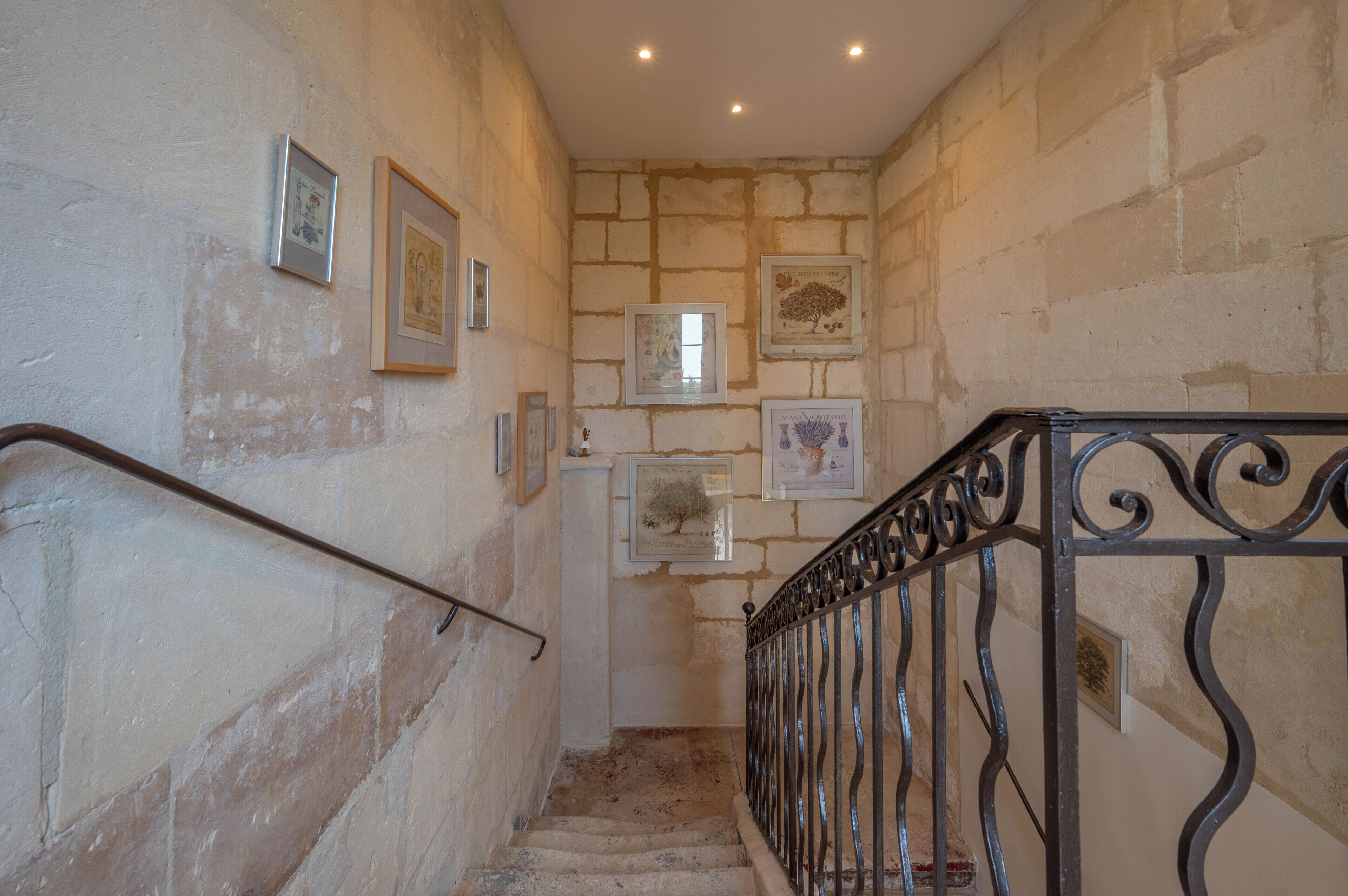 A staircase with stone walls and metal railings, leading to a landing with framed pictures.