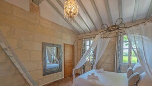 Un dormitorio con cama con dosel, una araña, un espejo y vista al jardín por la ventana.