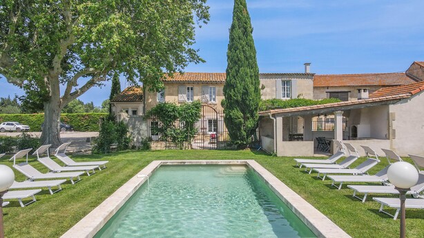 Una piscina con sillas de descanso, un edificio con techo de tejas y un árbol alto.