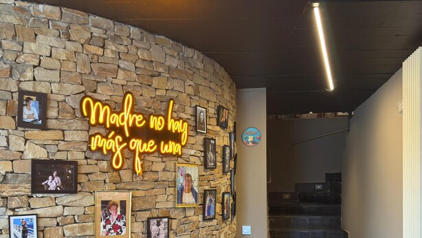 Un mur de pedra amb fotos enquadrades i un rètol de neó.