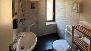 Un bany amb dutxa, rentapel, vàter i una finestra petita.