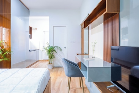 A modern bedroom with a bed, a desk, a chair, a mirror, and a potted plant.